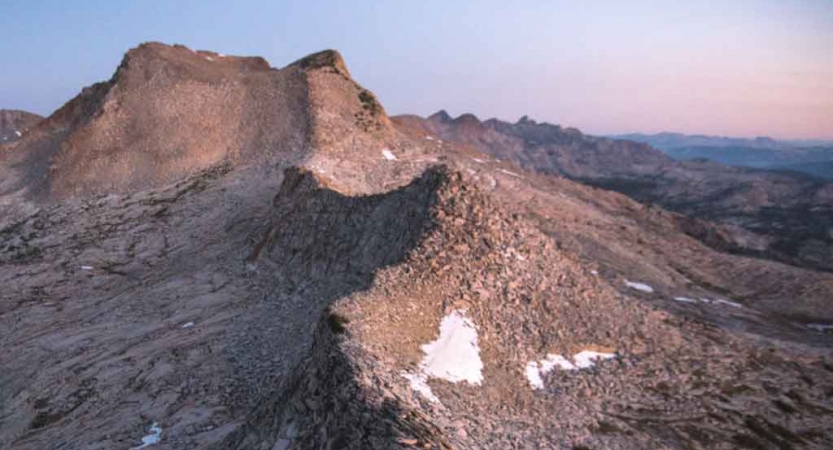 A mountainous ridge winds into the distance under a pink and purple sky.